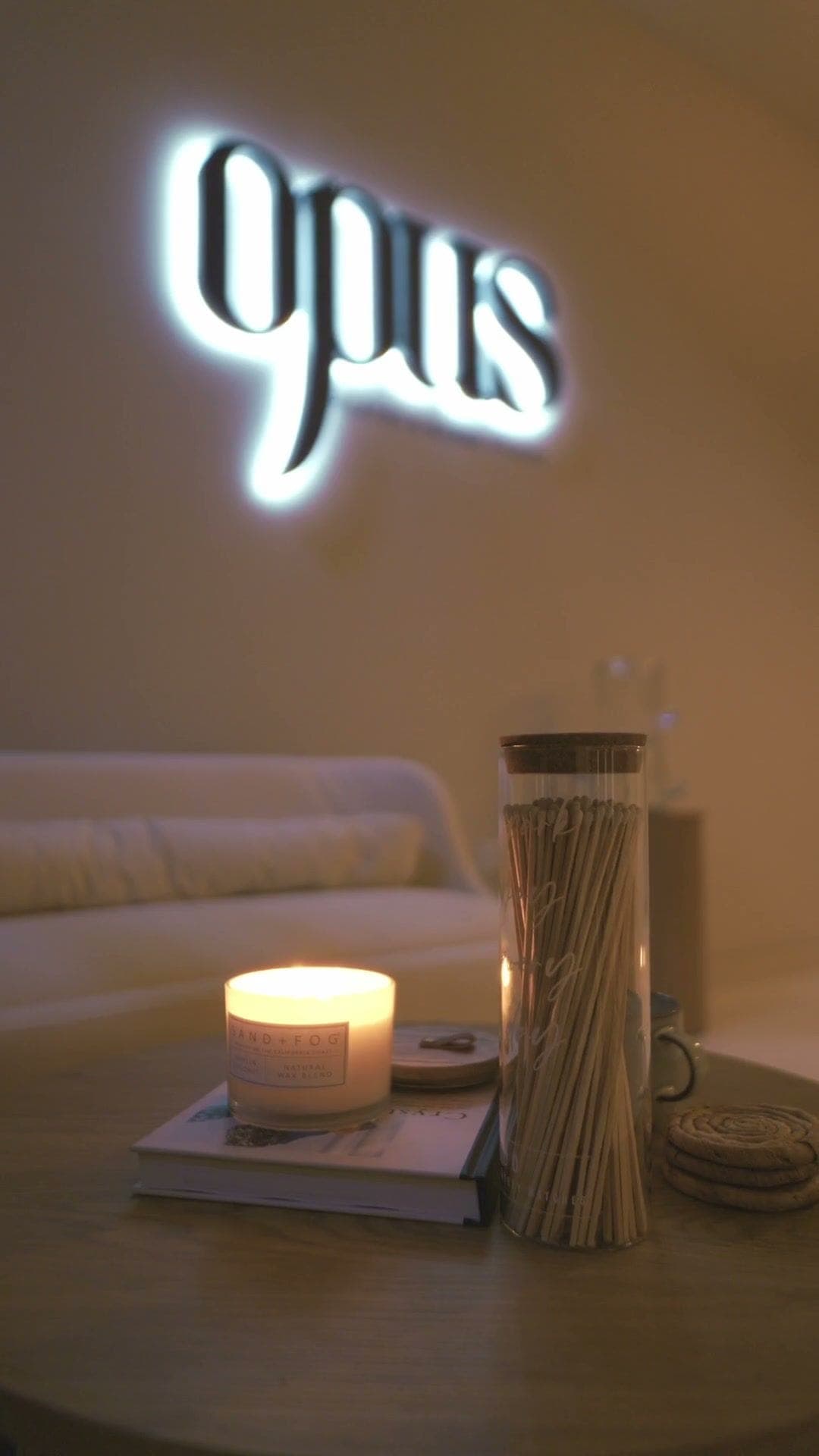 A lit candle on the lounge table under the glowing opus sign