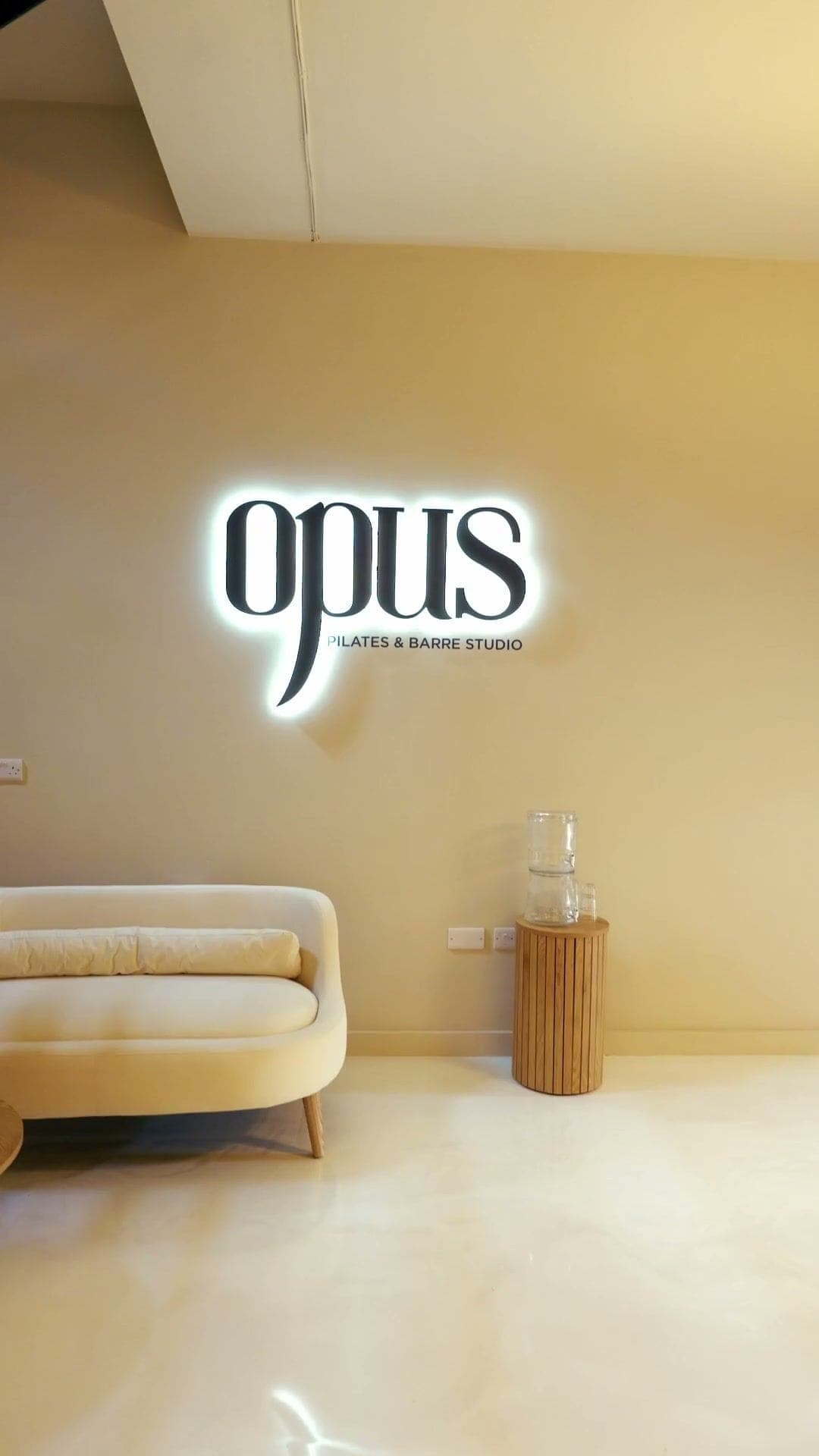 The lounge, with a curved cream sofa beneath the illuminated opus sign