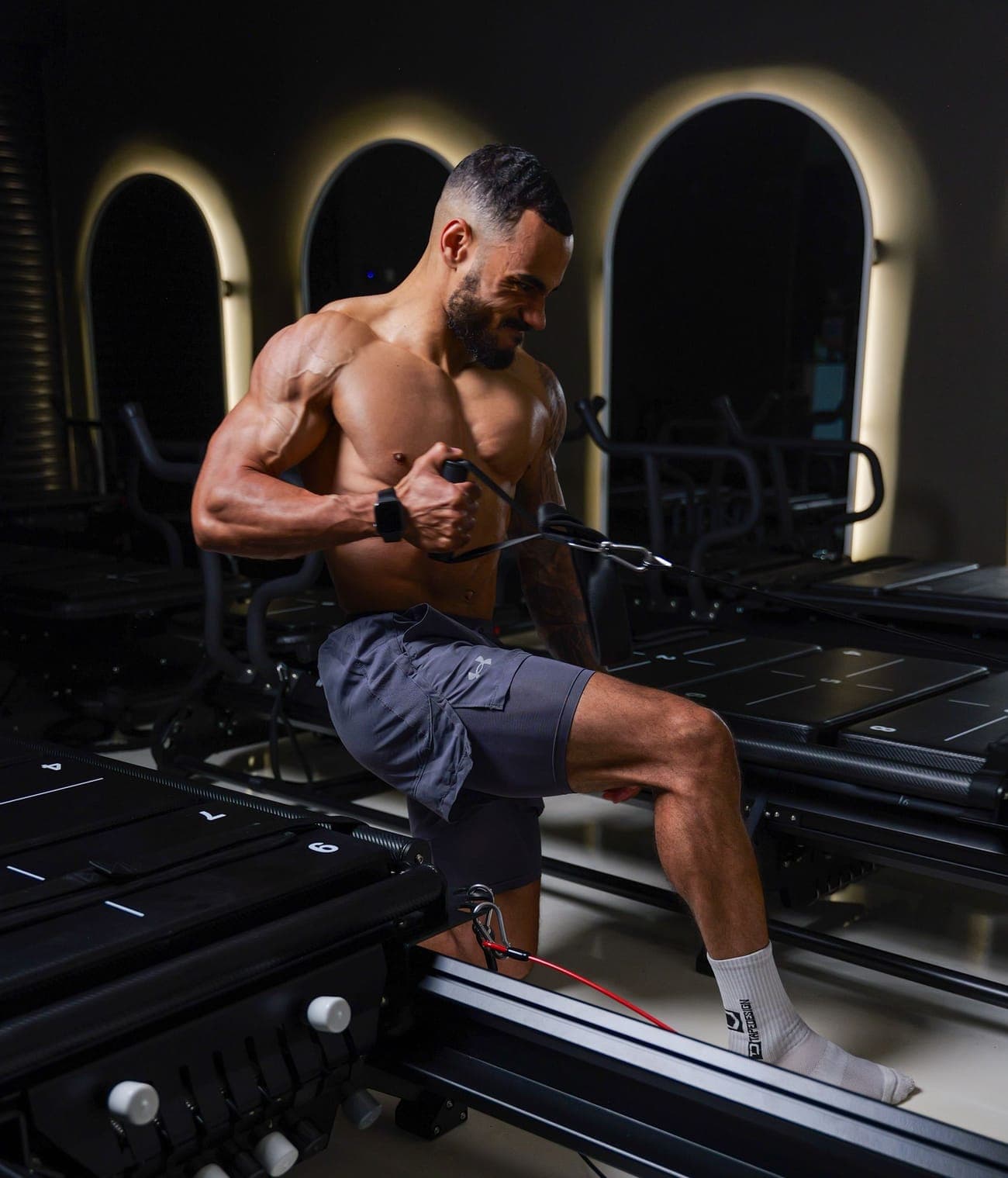 An INTENSE athlete mid-rep on a strength machine, cable in hand, under the lit arches